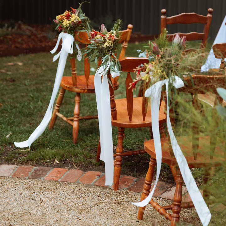 White satin ribbon tied to wooden chairs along aisle with native flowers