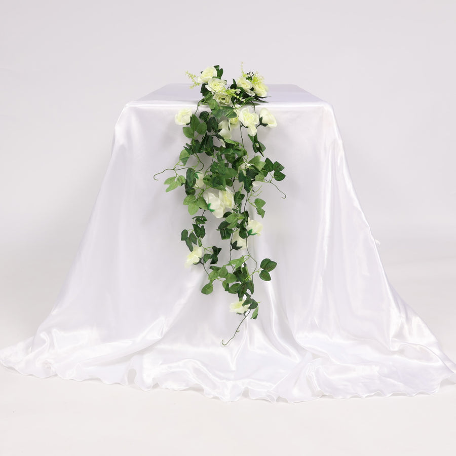 Artificial greenery and white flowers on a draped white fabric against a plain background
