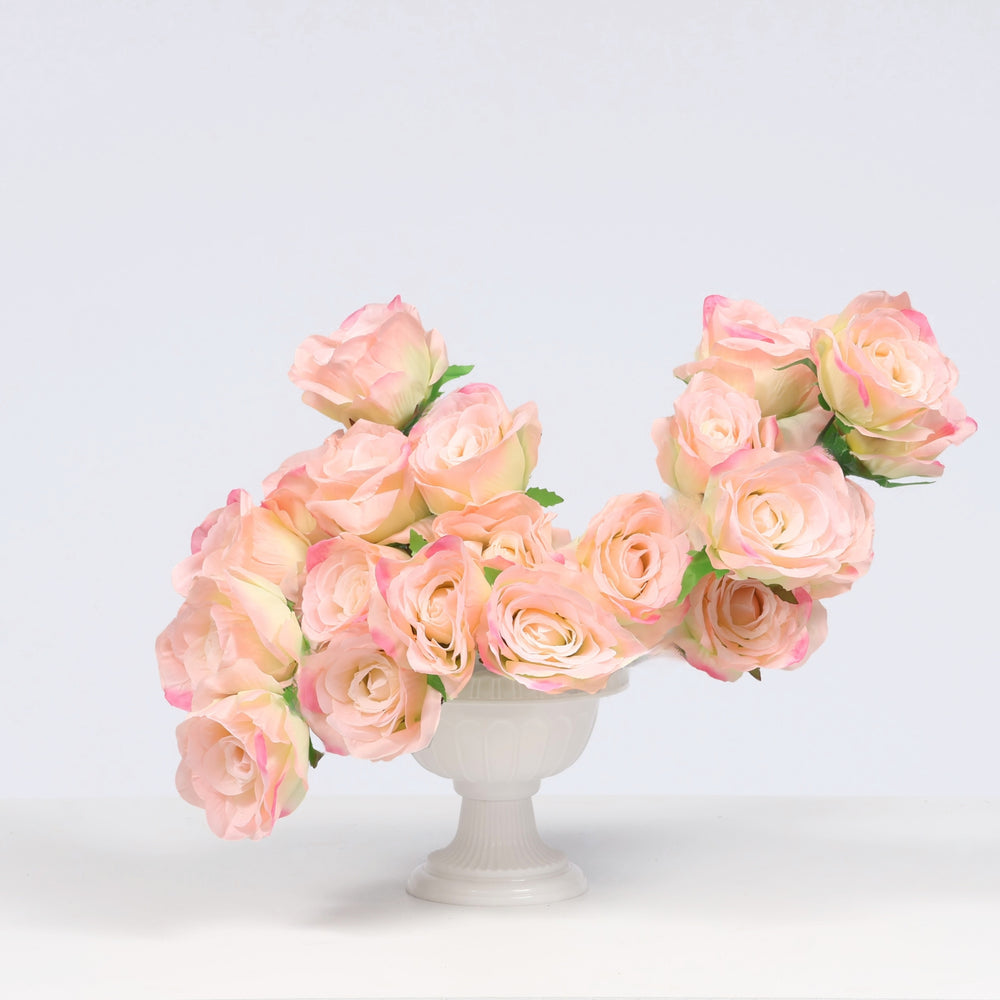 A bouquet of artificial pink roses arranged in a small white pedestal vase against a clean white studio background.