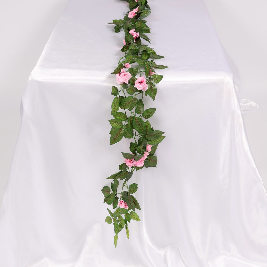 Artificial flower garland with pink flowers and green leaves on a white background