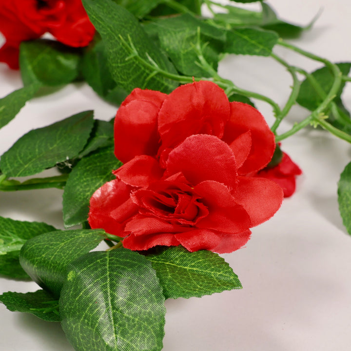 Red artificial roses with green leaves on a white background