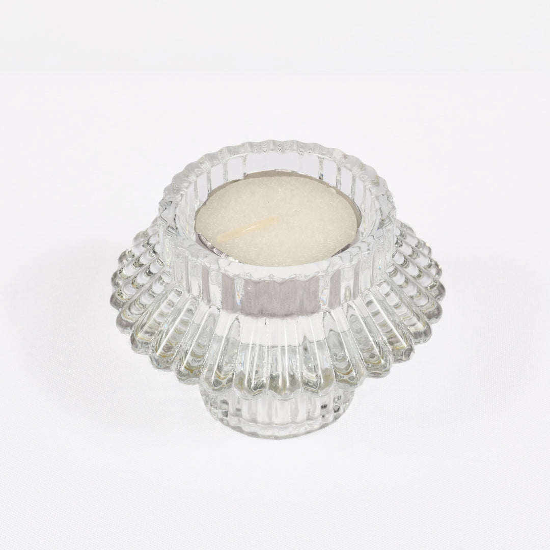 Clear glass candle holder with a white candle on a light grey background
