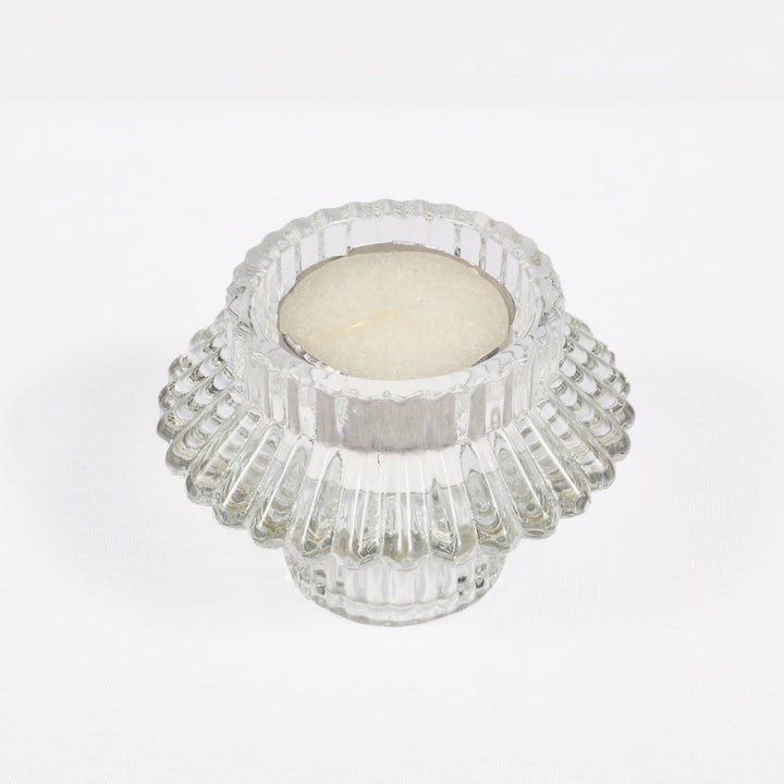 Clear glass candle holder with a white candle on a light grey background