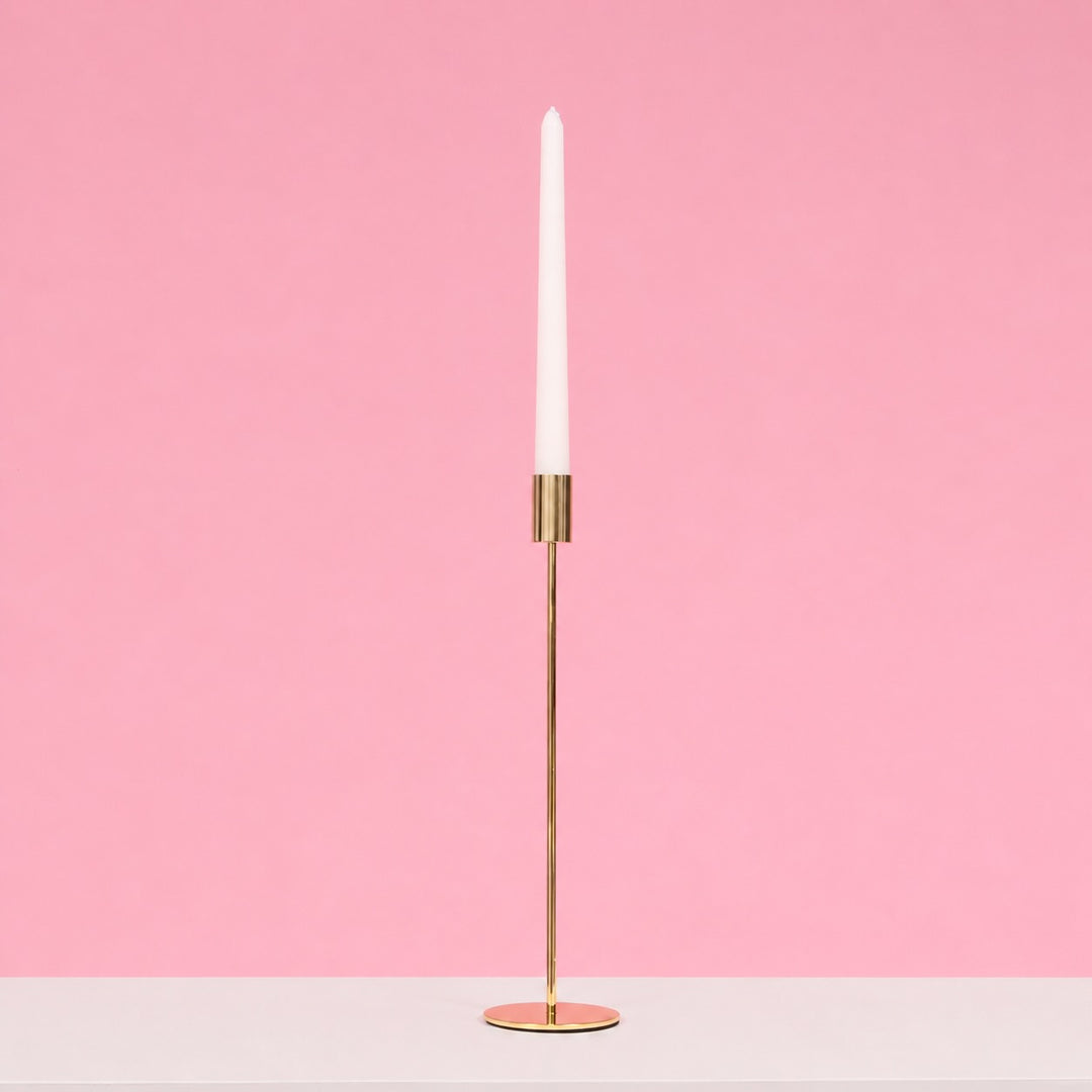 Gold candle holder with a white candle on a pink background