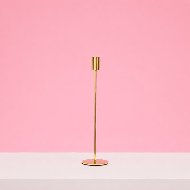 Gold candle holder on a white surface with a pink background
