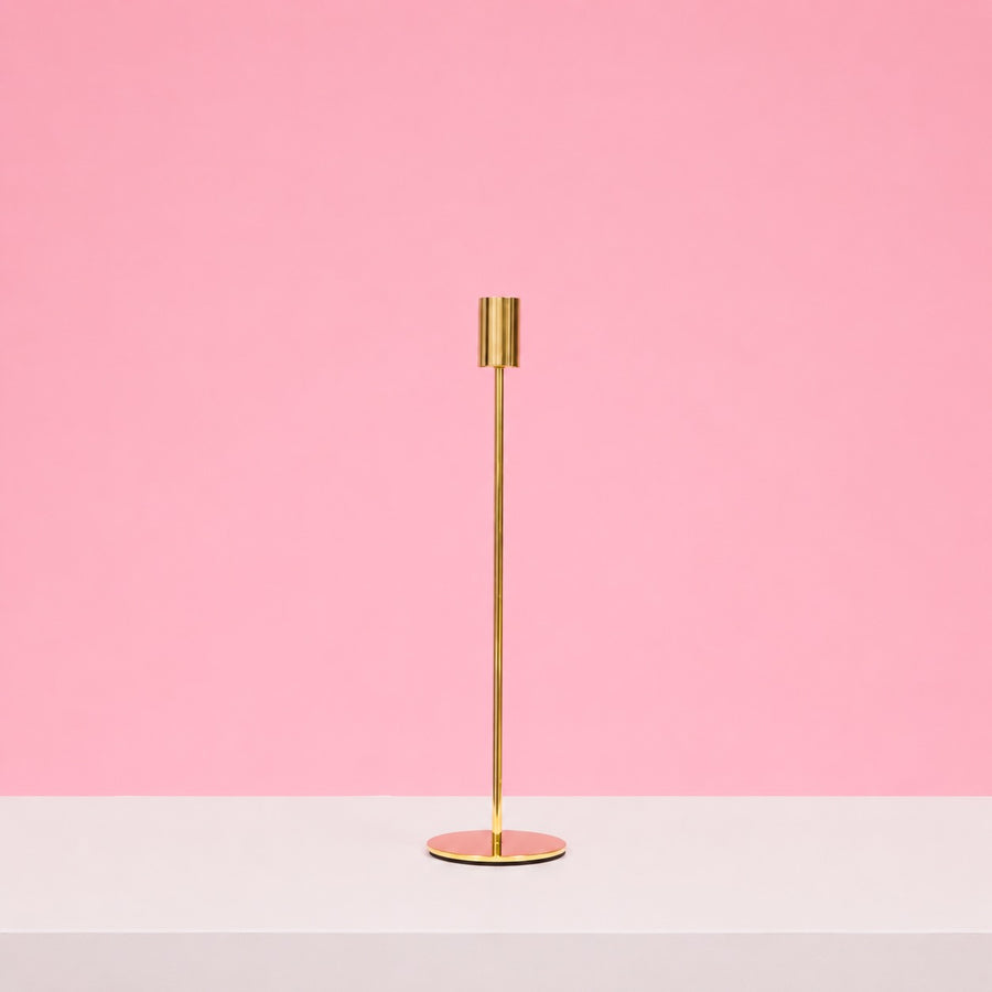 Gold candle holder on a white surface with a pink background