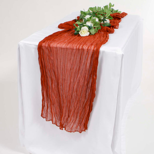 Rust Coloured Cheesecloth Table Runner on a white tablecloth with greenery