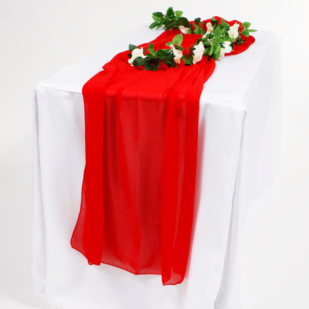 Red chiffon table runner, on a white tablecloth, with greenery