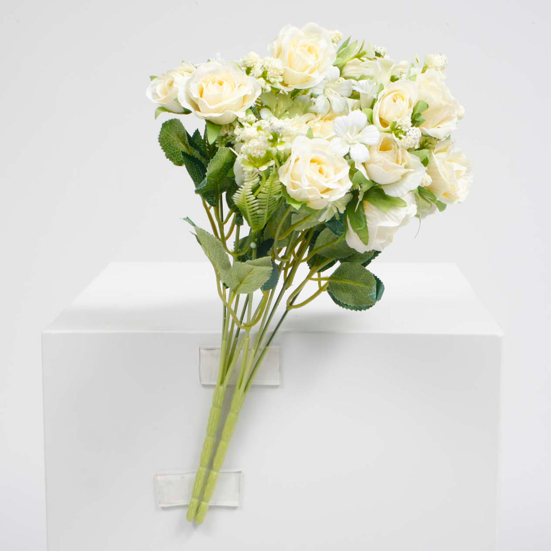 An artificial flower bouquet featuring cream-colored roses and green leaves, displayed on a white block against a light gray background.