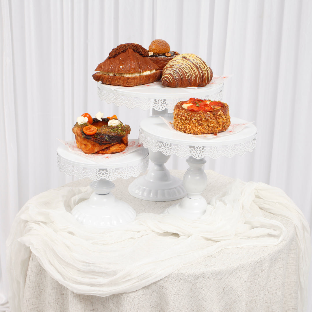 White lace vintage cake stand set with pastries on top of a round table with a white chiffon table runner draped over a linen tablecloth