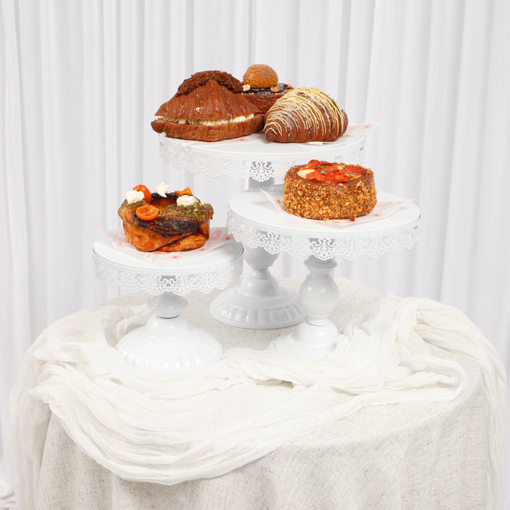 White lace vintage cake stand set with pastries on top of a round table with a white chiffon table runner draped over a linen tablecloth