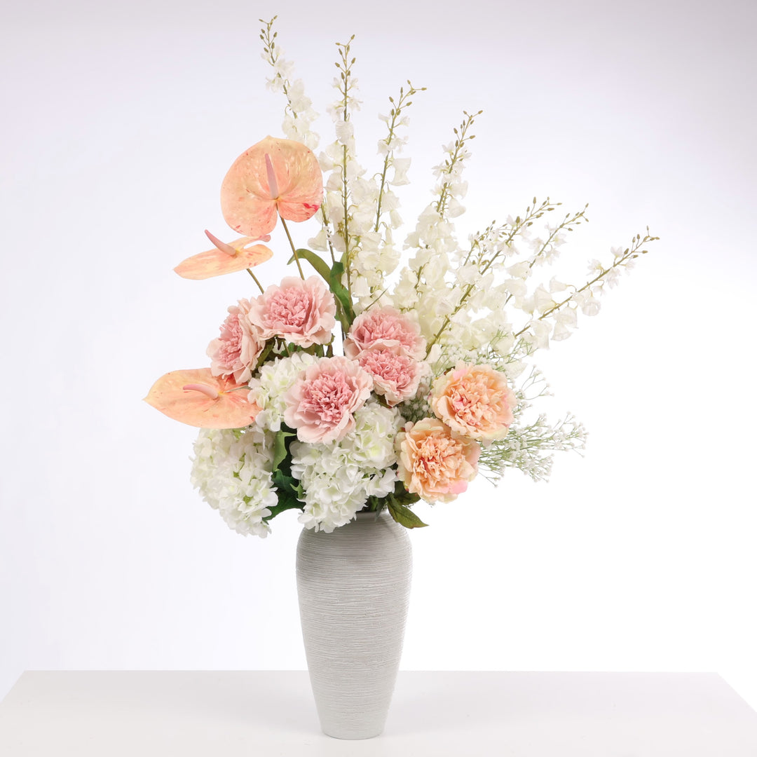 Flower arrangement made up of White Hydrangeas, Peach Anthurium, White Foxglove, White Babys Breath, Blush and Peach Peony Roses displayed in Textured Centrepiece Urn Shaped Vase - Light Grey (18x34cm)