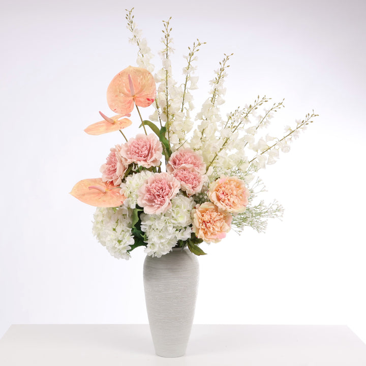 Flower arrangement made up of White Hydrangeas, Peach Anthurium, White Foxglove, White Babys Breath, Blush and Peach Peony Roses displayed in Textured Centrepiece Urn Shaped Vase - Light Grey (18x34cm)