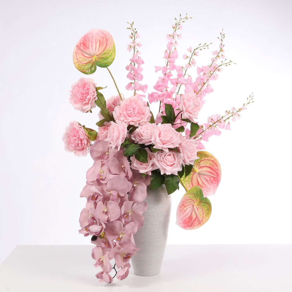 Pink flower arrangement made up of Orchids, Peony Roses, Anthurium, Roses and Foxglove stems displayed in Textured Centrepiece Urn Shaped Vase - Light Grey (18x34cm)