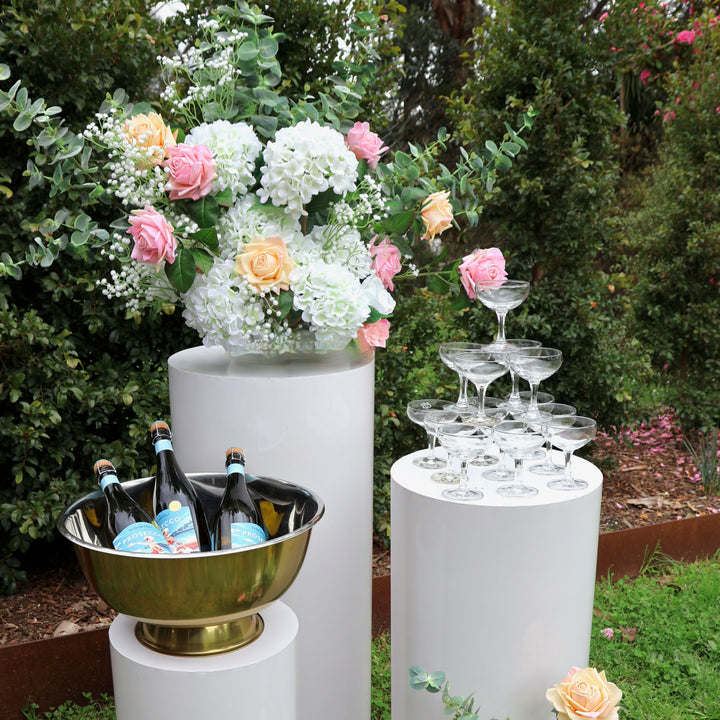 Round plinth set with prosecco in cooler, champagne coupe tower and flower arrangement with hydrangeas, roses, eucalyptus and baby's breath.