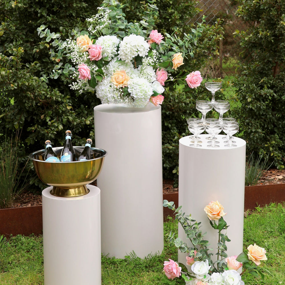 White round plinth set with prosecco in cooler, coupe champagne glasses stacked in a tower and flower arrangements made with hydrangea stems, roses, eucalyptus and baby's breath.