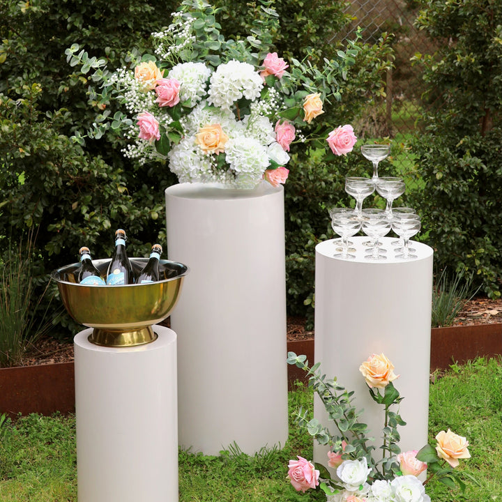 White round plinth set with prosecco in cooler, coupe champagne glasses stacked in a tower and flower arrangements made with hydrangea stems, roses, eucalyptus and baby's breath.