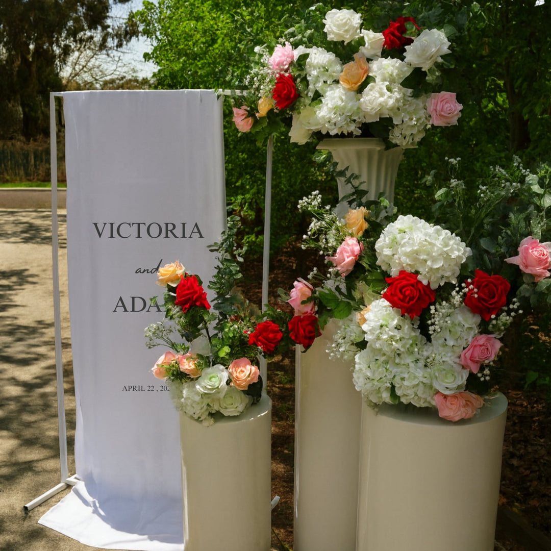 Welcome sign with round white plinth set, roses, hydrangeas, eucalyptus and baby's breath arrangements.