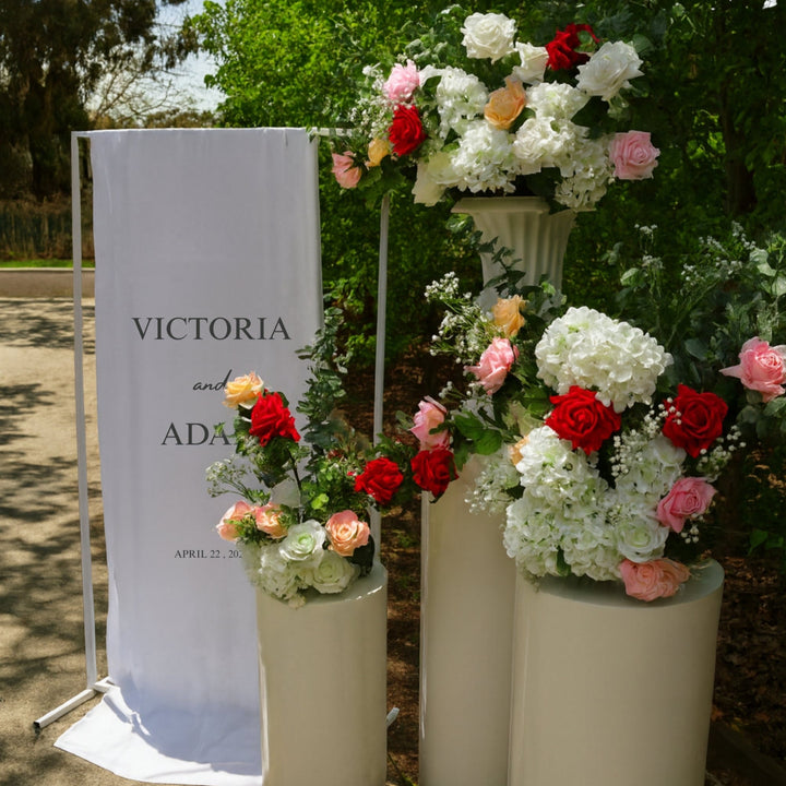 Welcome sign with round white plinth set, roses, hydrangeas, eucalyptus and baby's breath arrangements.