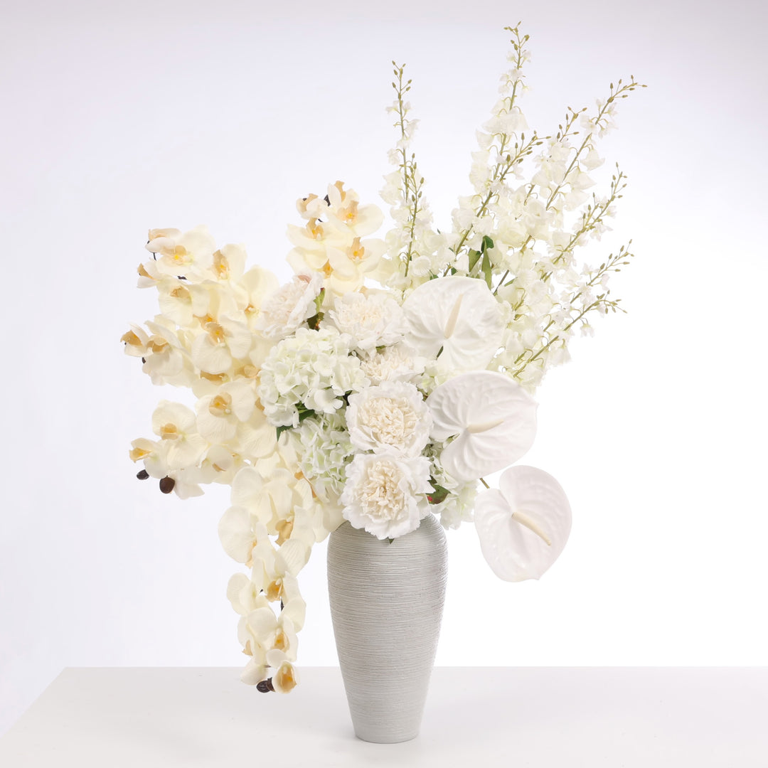White arrangement of flowers - Orchids, Peony Roses, Hydrangeas, Anthurium and Foxglove stems displayed in Textured Centrepiece Urn Shaped Vase - Light Grey (18x34cm)